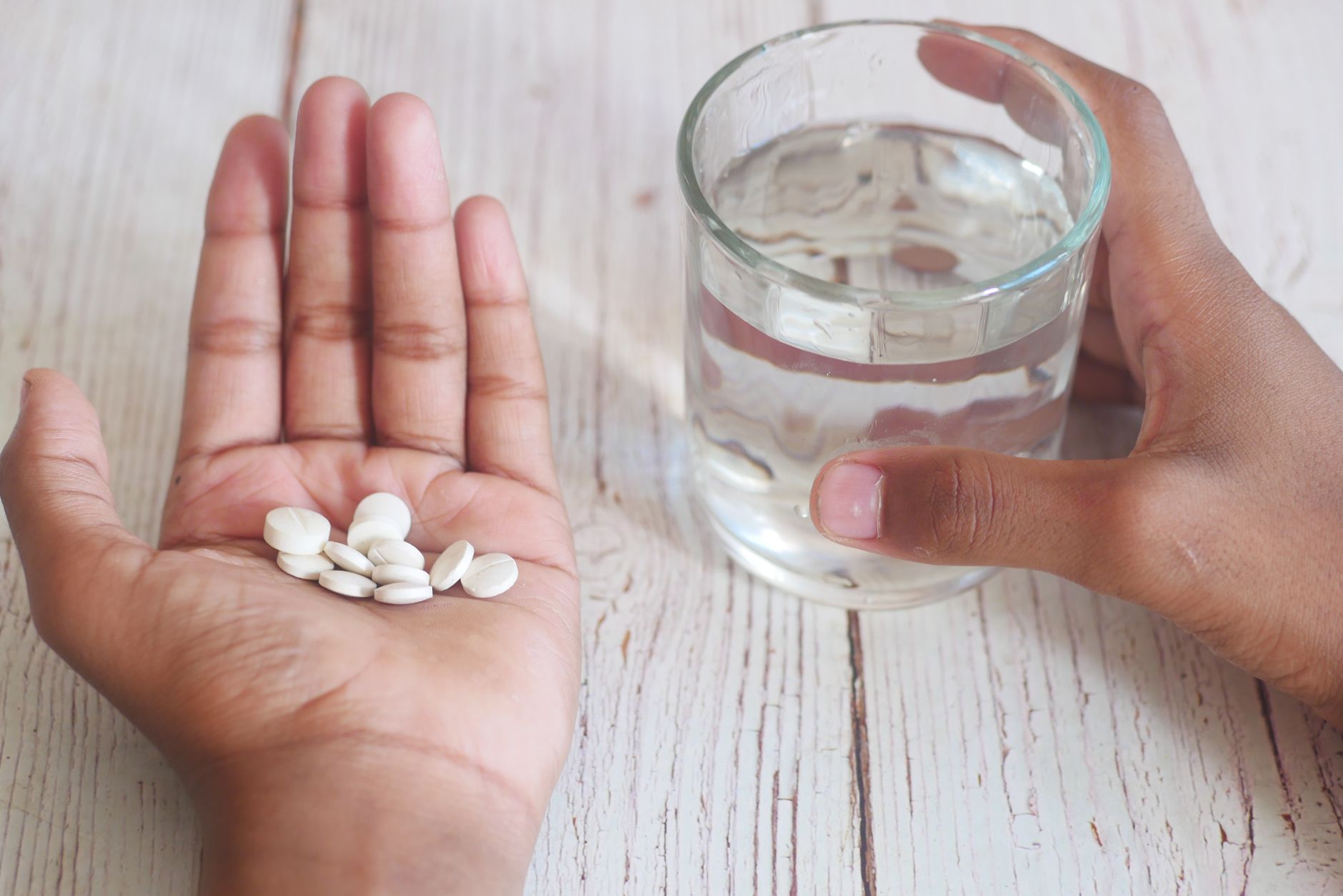 Weiße Tabletten in einer geöffneten Handfläche neben einem Glas Wasser
