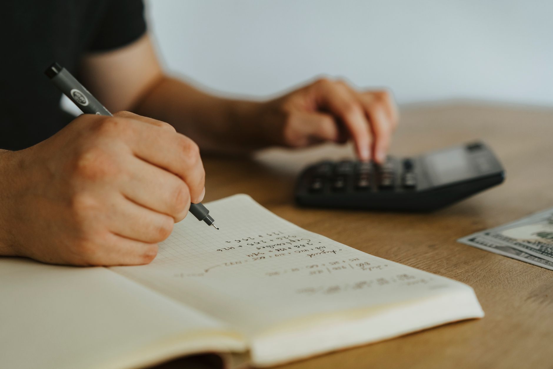 Hände mit Notizbuch, Stift und Taschenrechner beim Nachrechnen