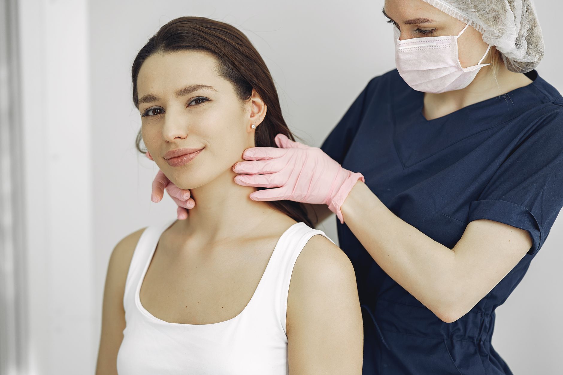 Medizinische Fachkraft mit Handschuhen tastet den Hals einer Patientin ab.