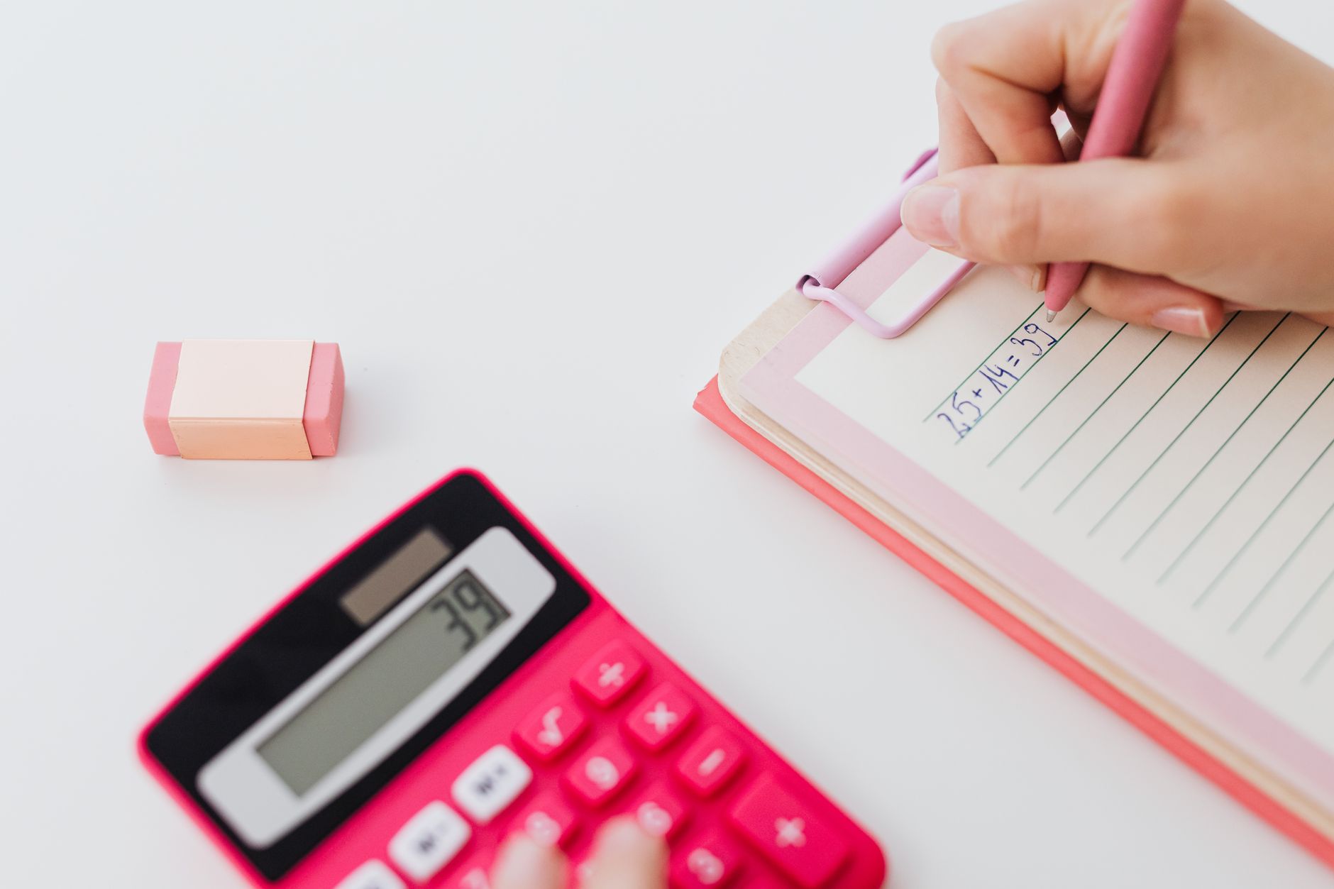 A hand adding two figures on a notepad, a calculator beside it