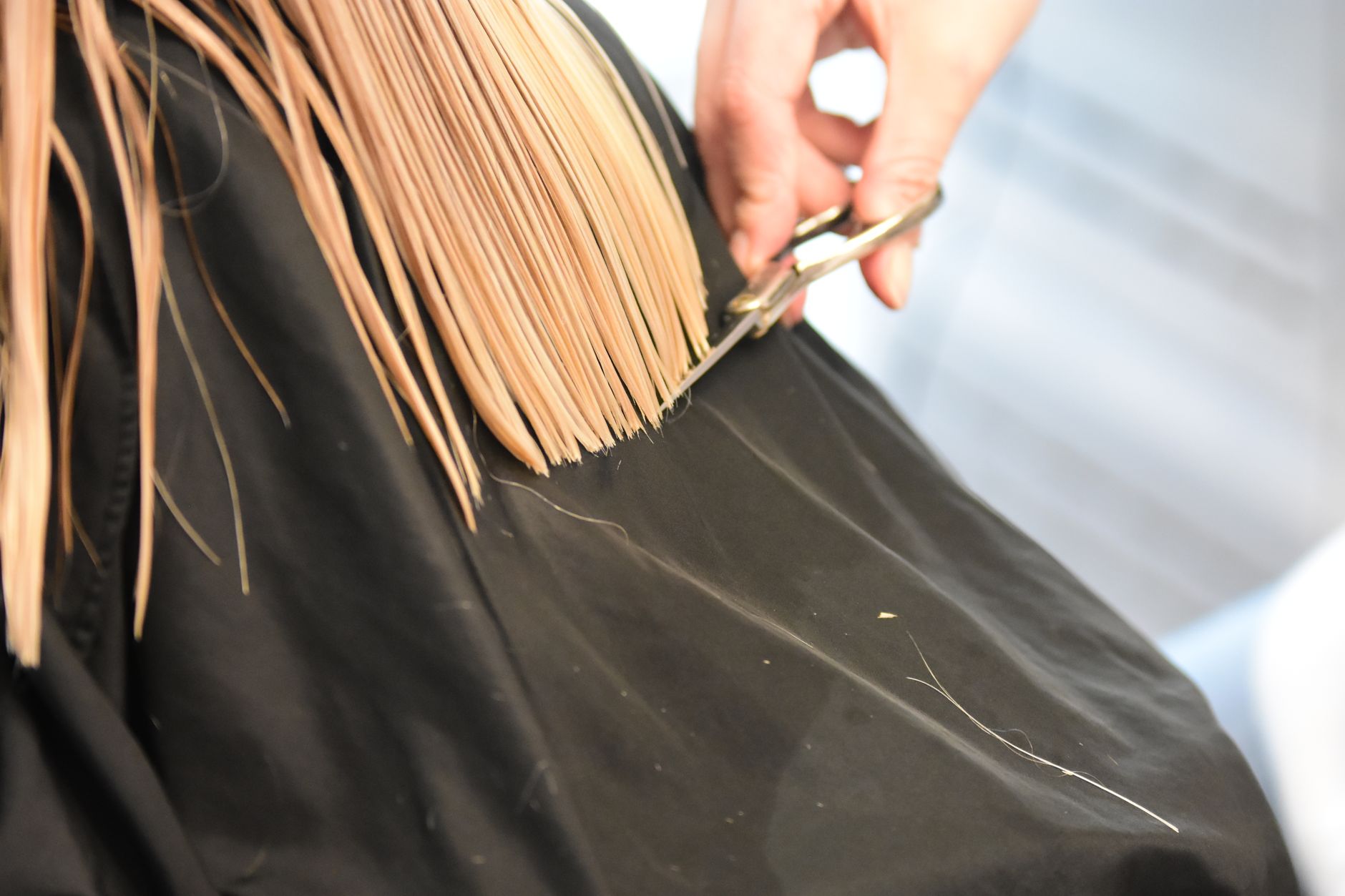 Friseurin schneidet blondes Haar mit einer Schere, Nahaufnahme