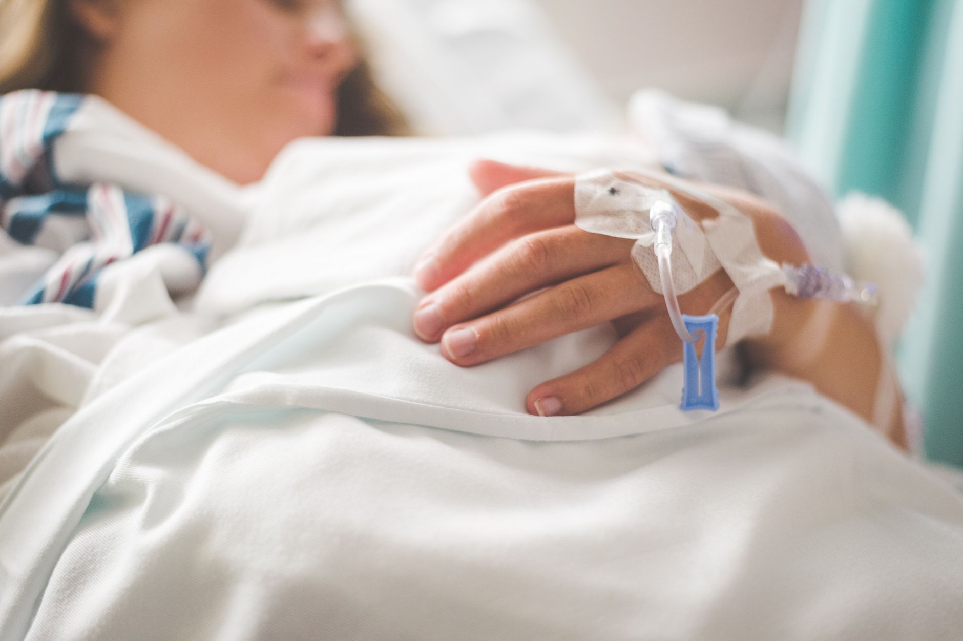 Hand einer Patientin mit Infusionszugang im Krankenhausbett