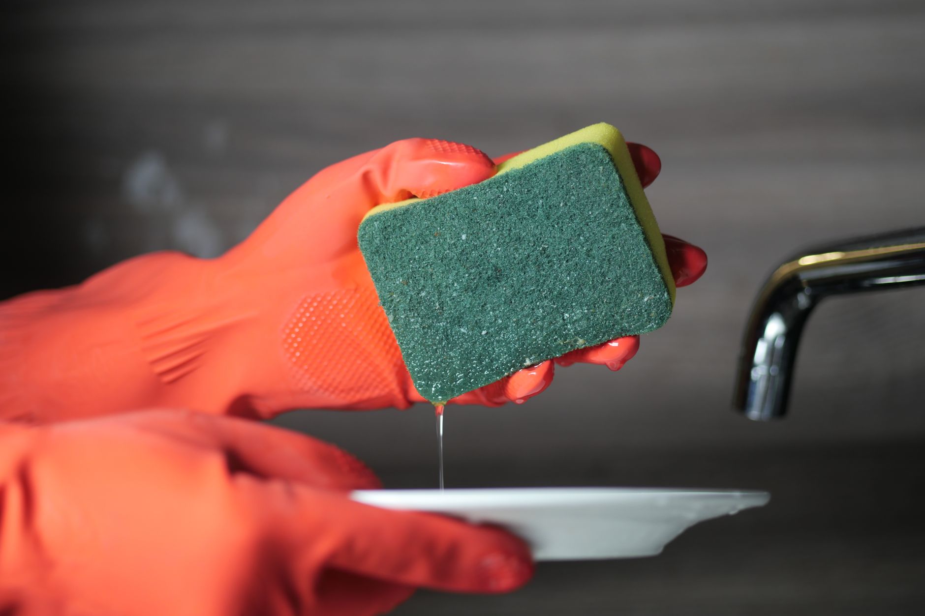Hände in Gummihandschuhen beim Spülen am Waschbecken