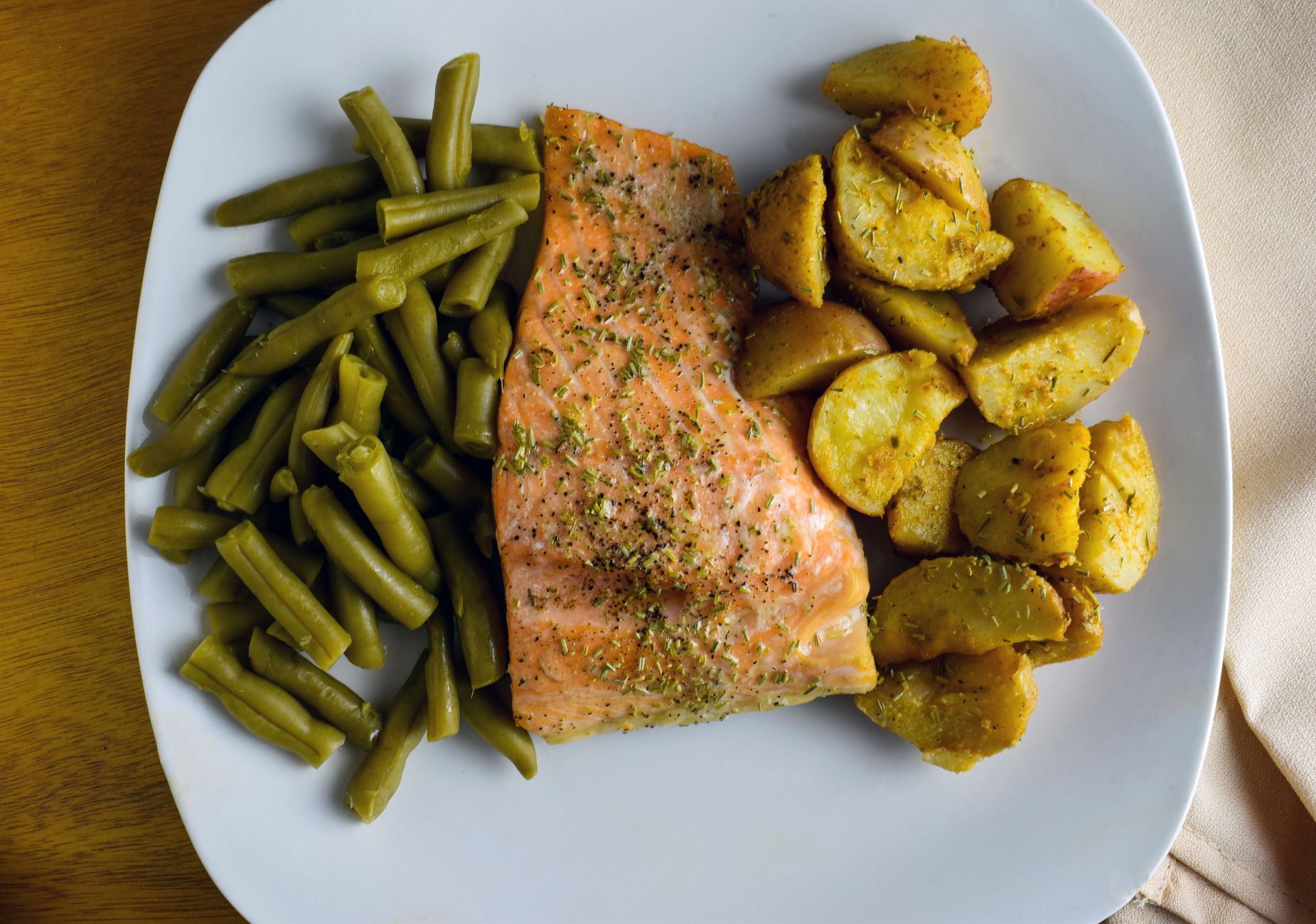 Lachsfilet mit grünen Bohnen und Röstkartoffeln auf einem weißen Teller