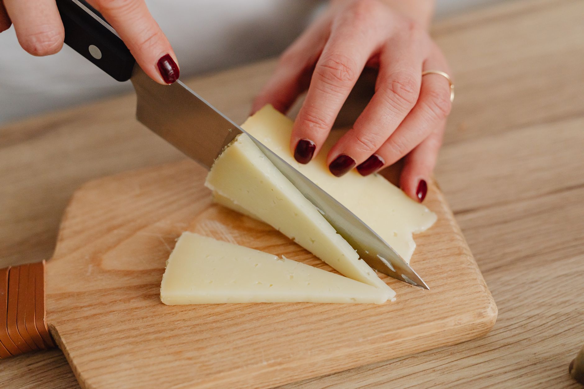 Hartkäse wird auf einem Holzbrett in Scheiben geschnitten