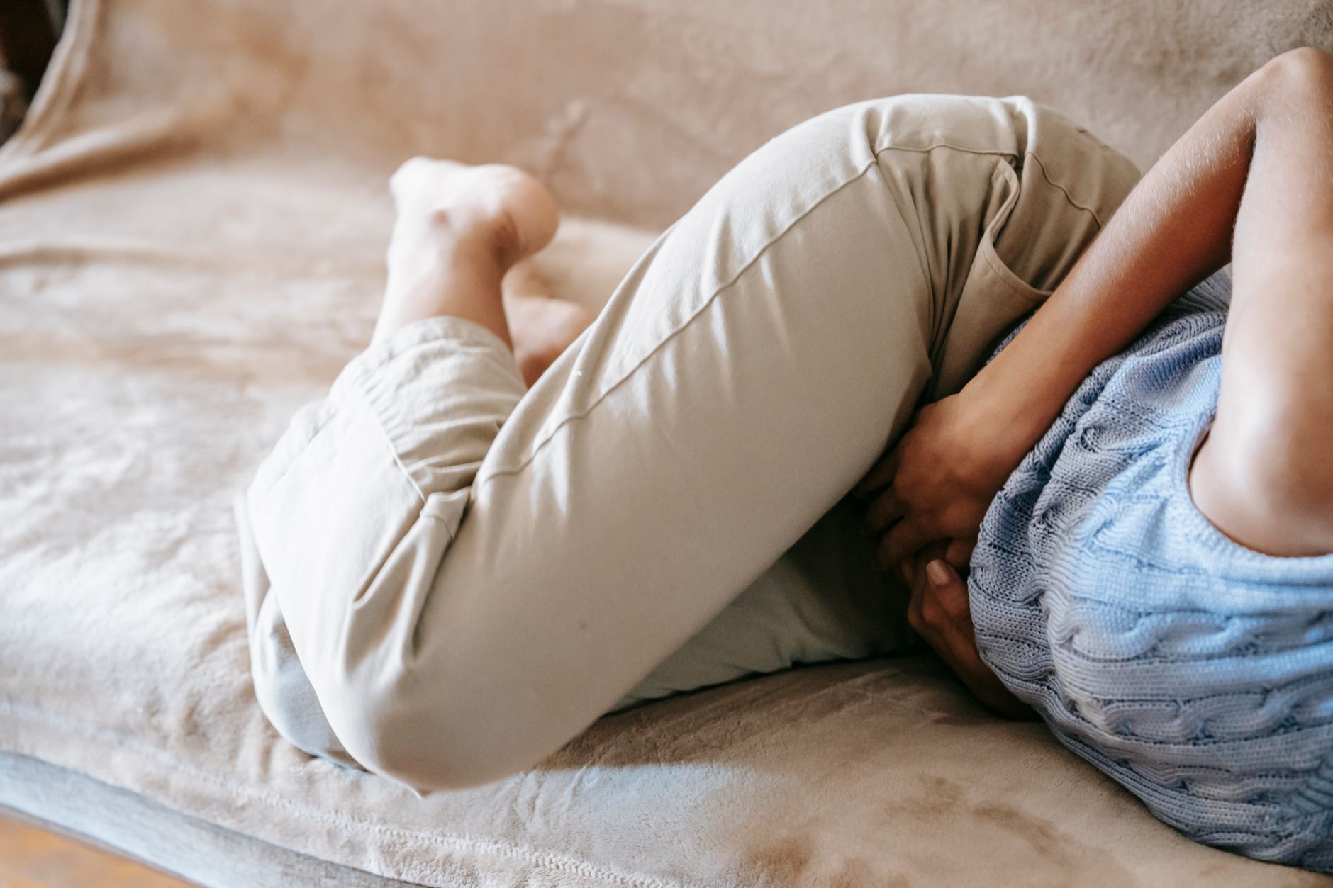 Person liegt zusammengerollt mit Bauchschmerzen auf einer Couch