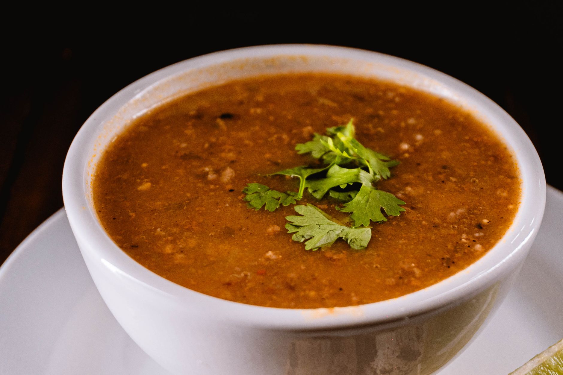 Weiße Schale mit dicker brauner Suppe, garniert mit frischen Korianderblättern