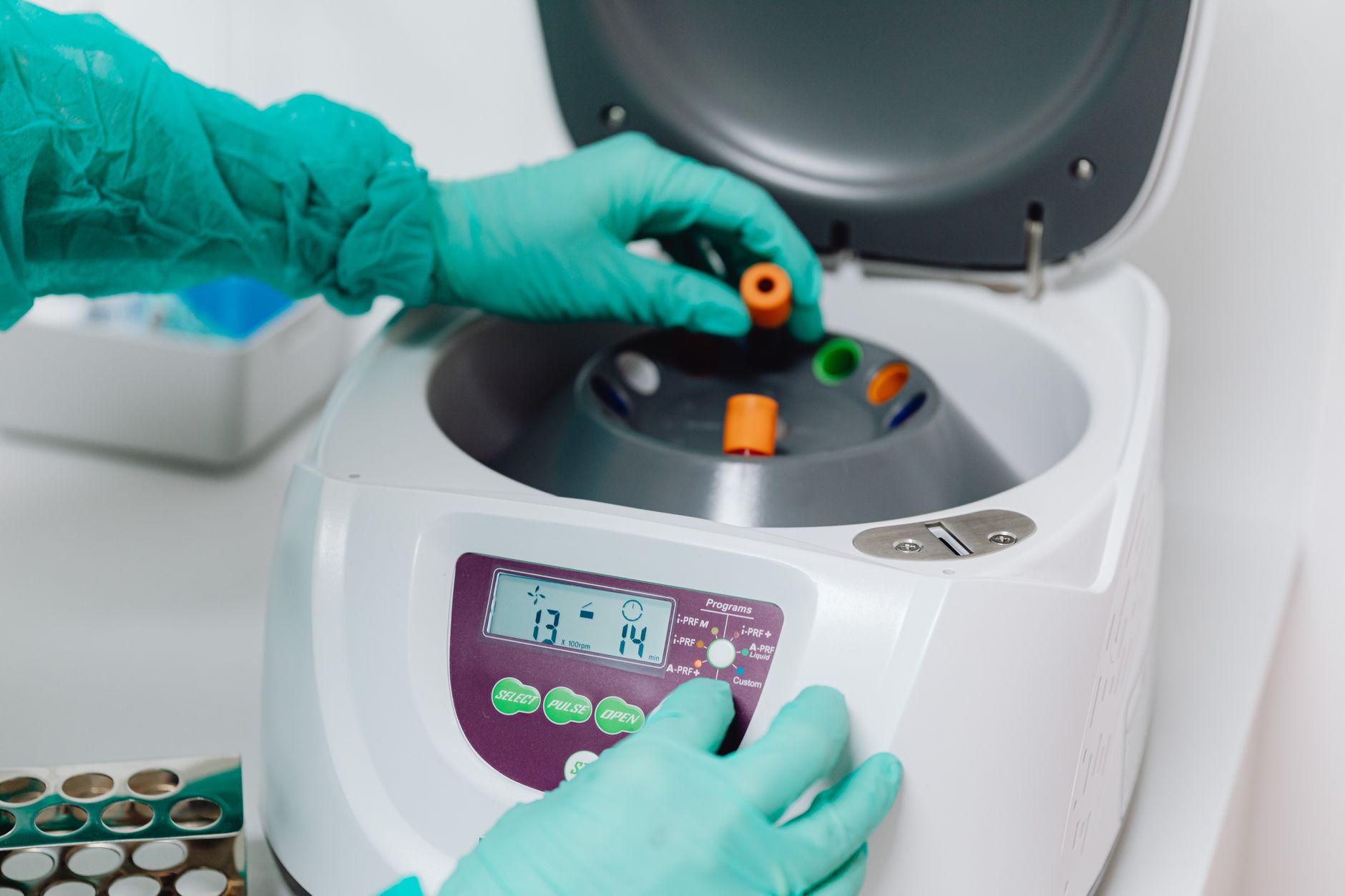 Une main gantée de vert place un tube d'échantillon dans une centrifugeuse de laboratoire
