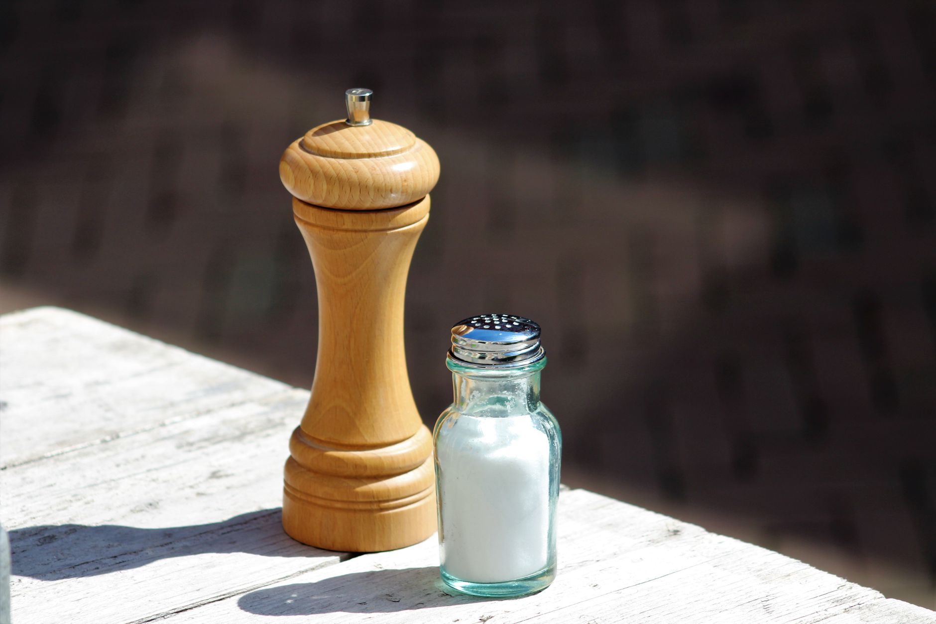 Ein Glassalzstreuer und eine hölzerne Pfeffermühle auf einem sonnenbeschienenen Holztisch