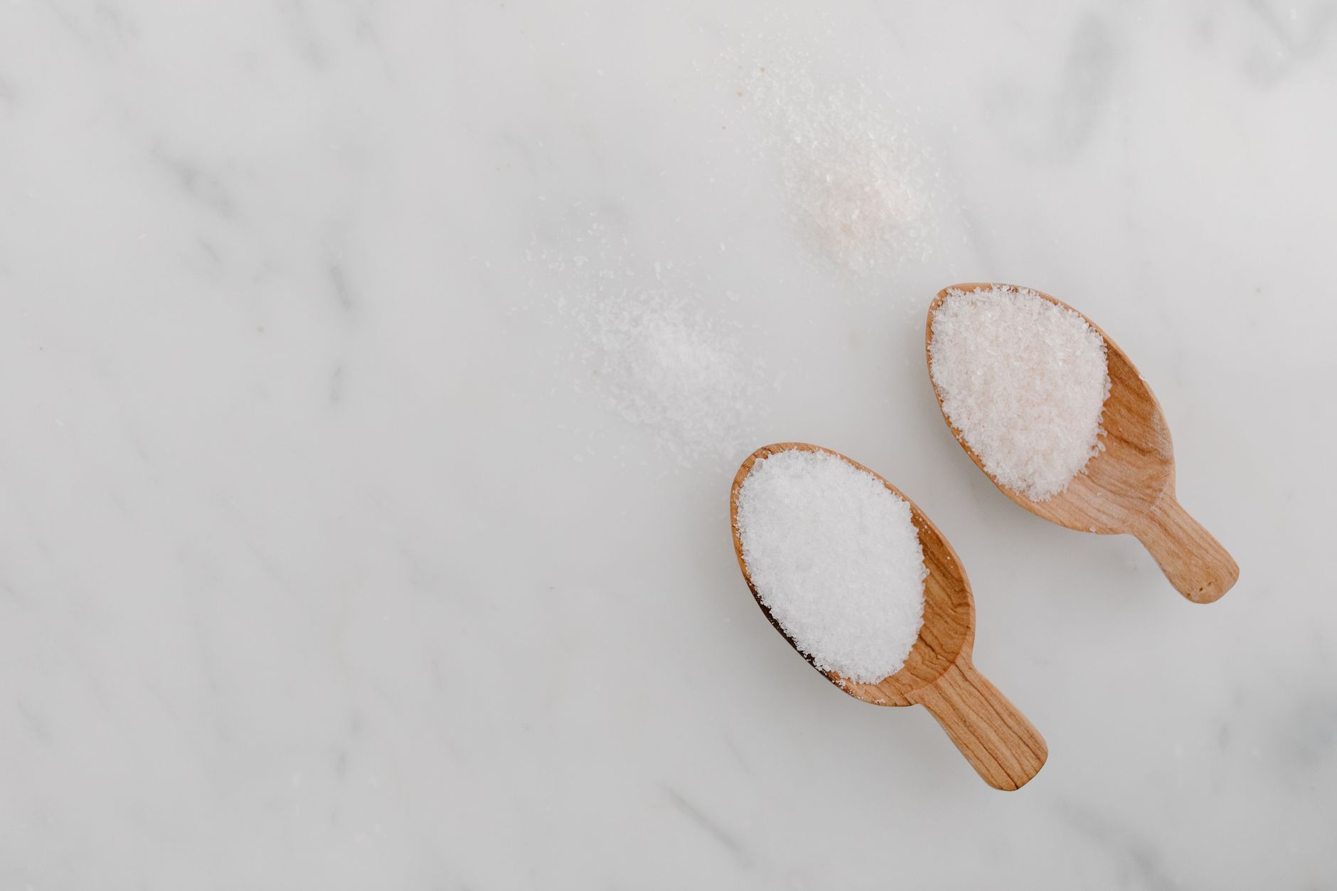 Due palette di legno colme di sale bianco su un piano di marmo, alcuni granelli accanto