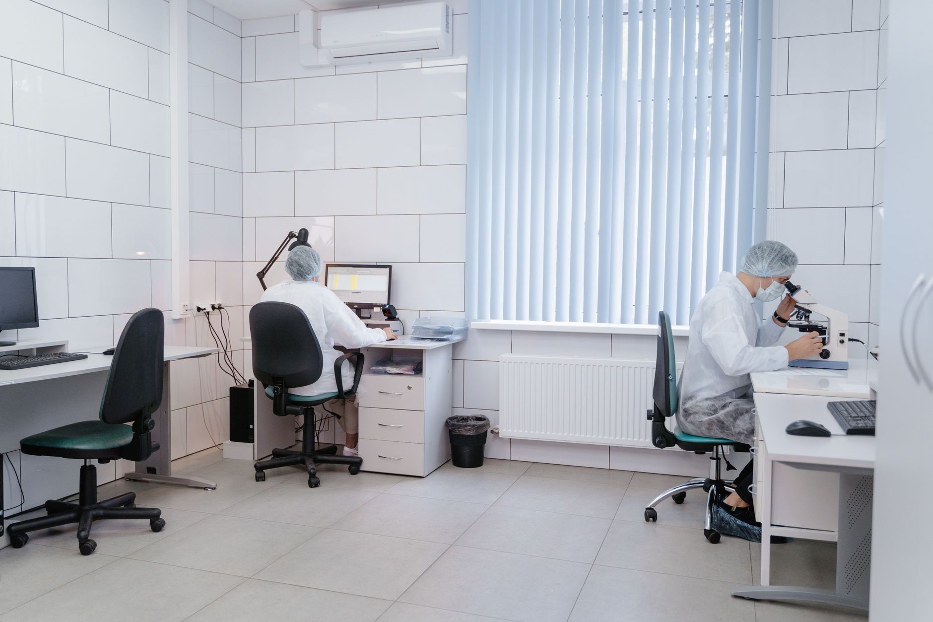Zwei Laborantinnen in einem hellen Labor arbeiten an Mikroskopen und Rechnern