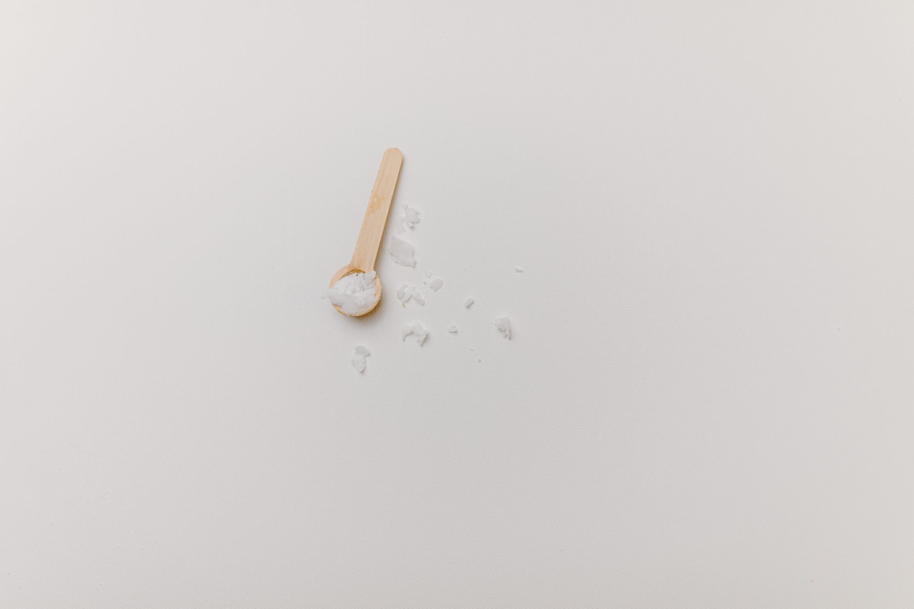 Ein sehr kleiner Holzlöffel mit etwas weißem Pulver auf hellem Untergrund