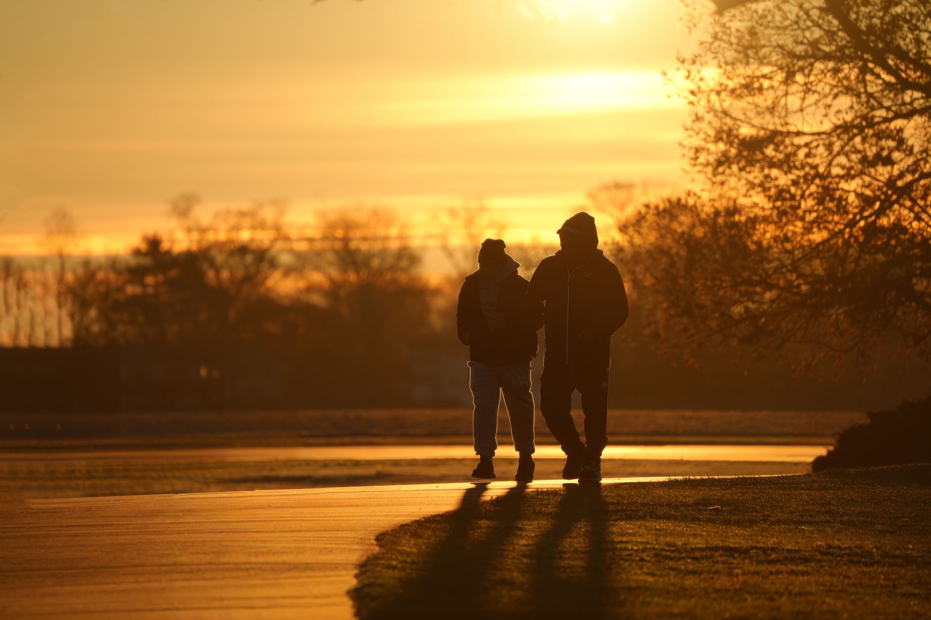 Zwei Menschen gehen bei tief stehender Morgensonne einen Weg entlang