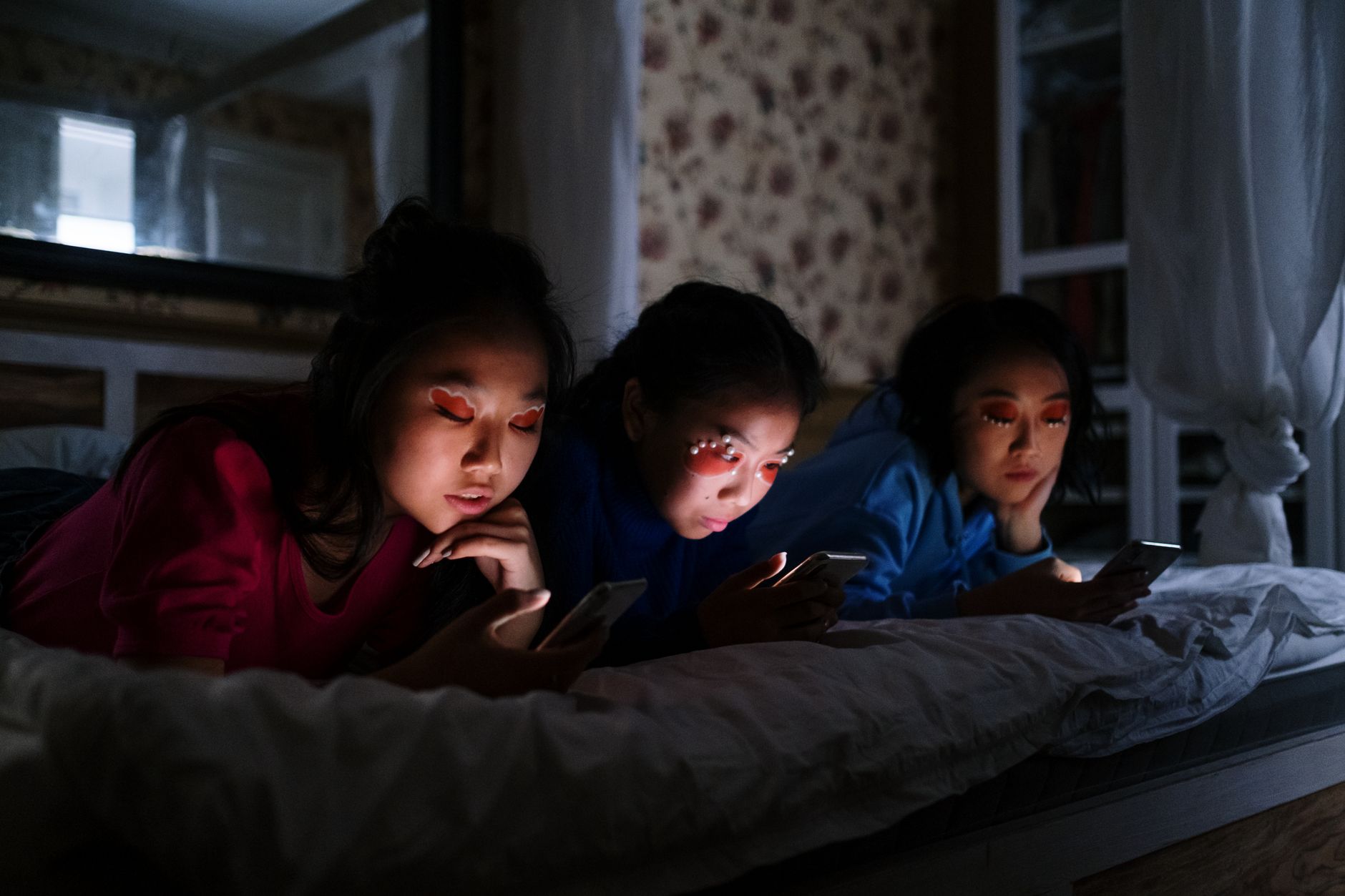Drei Jugendliche liegen im dunklen Zimmer auf einem Bett und schauen auf ihre Smartphones