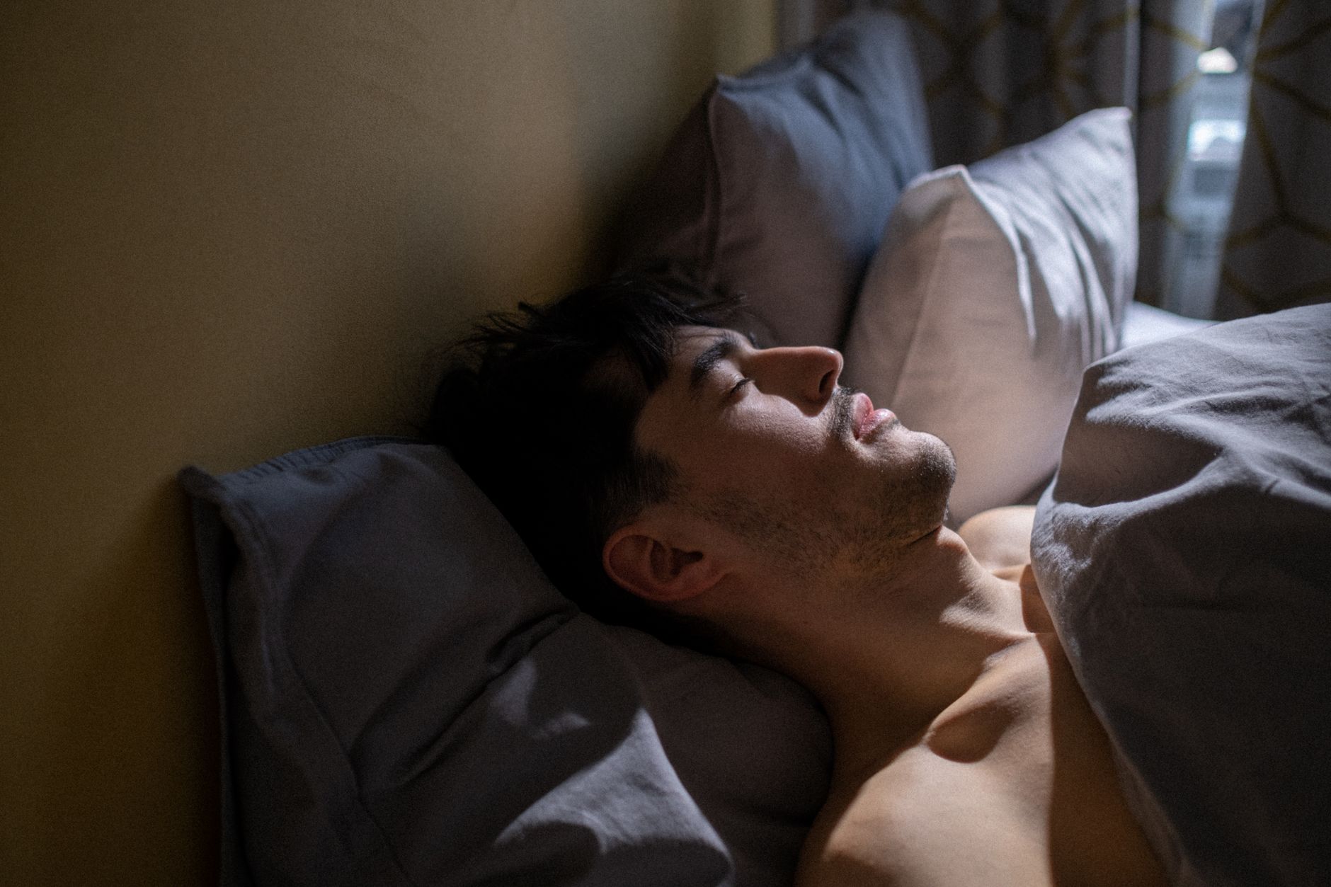Mann schläft am Vormittag in einem abgedunkelten Schlafzimmer