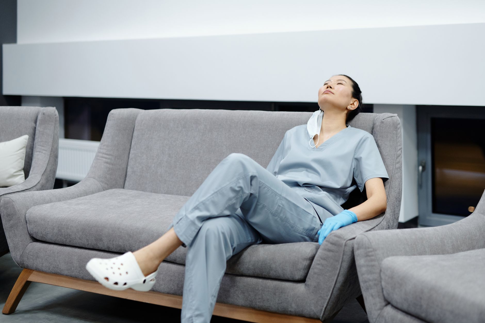 Pflegekraft in Kasack ruht nach der Schicht auf einem Sofa