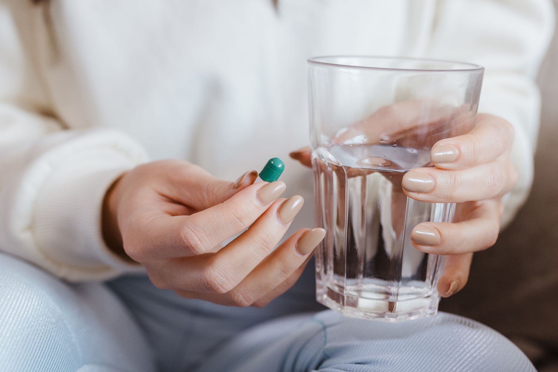 Hände halten eine Kapsel und ein Glas Wasser