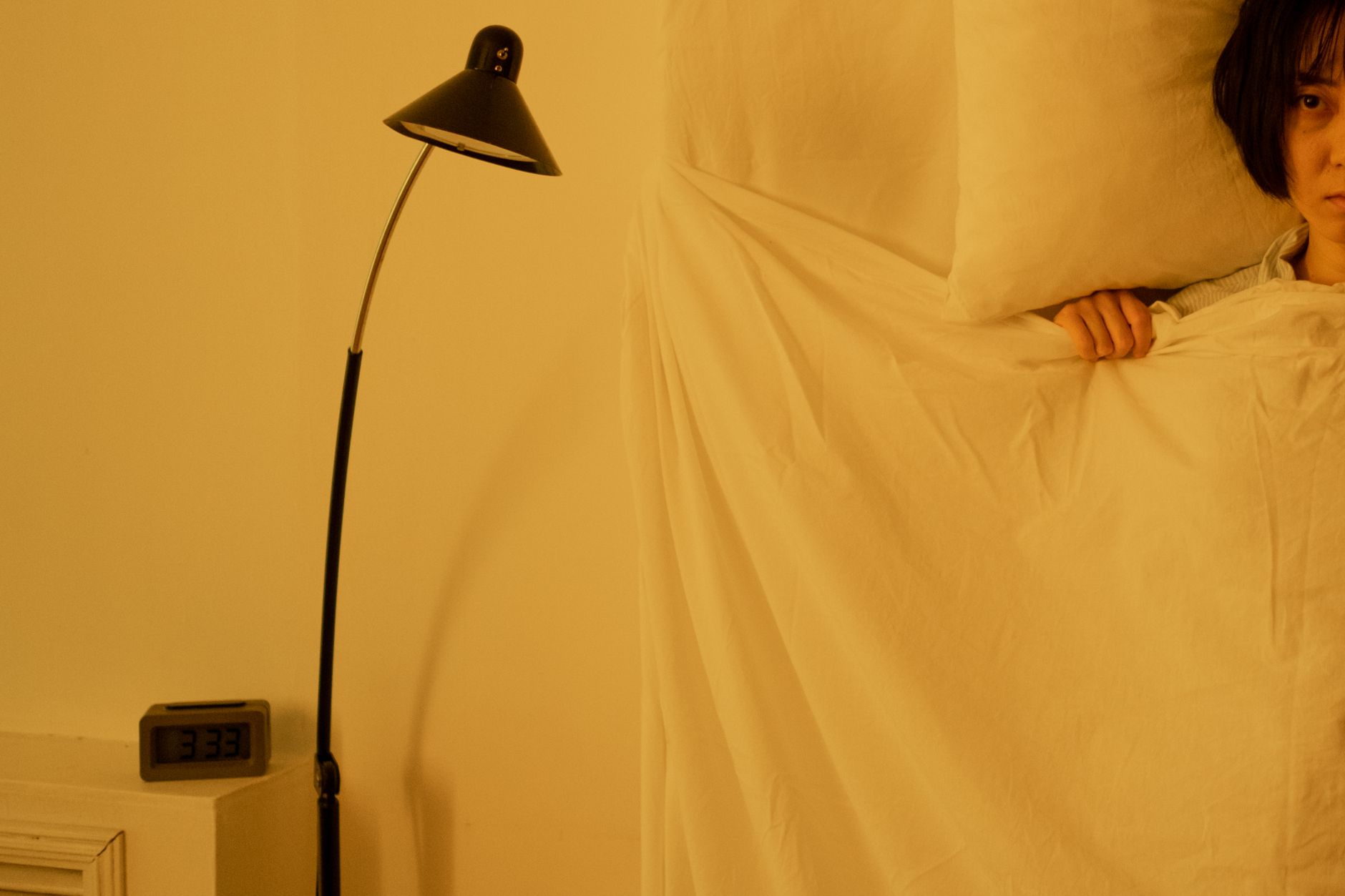Digitaler Wecker zeigt 3:33 Uhr, dahinter eine wache Person im Bett