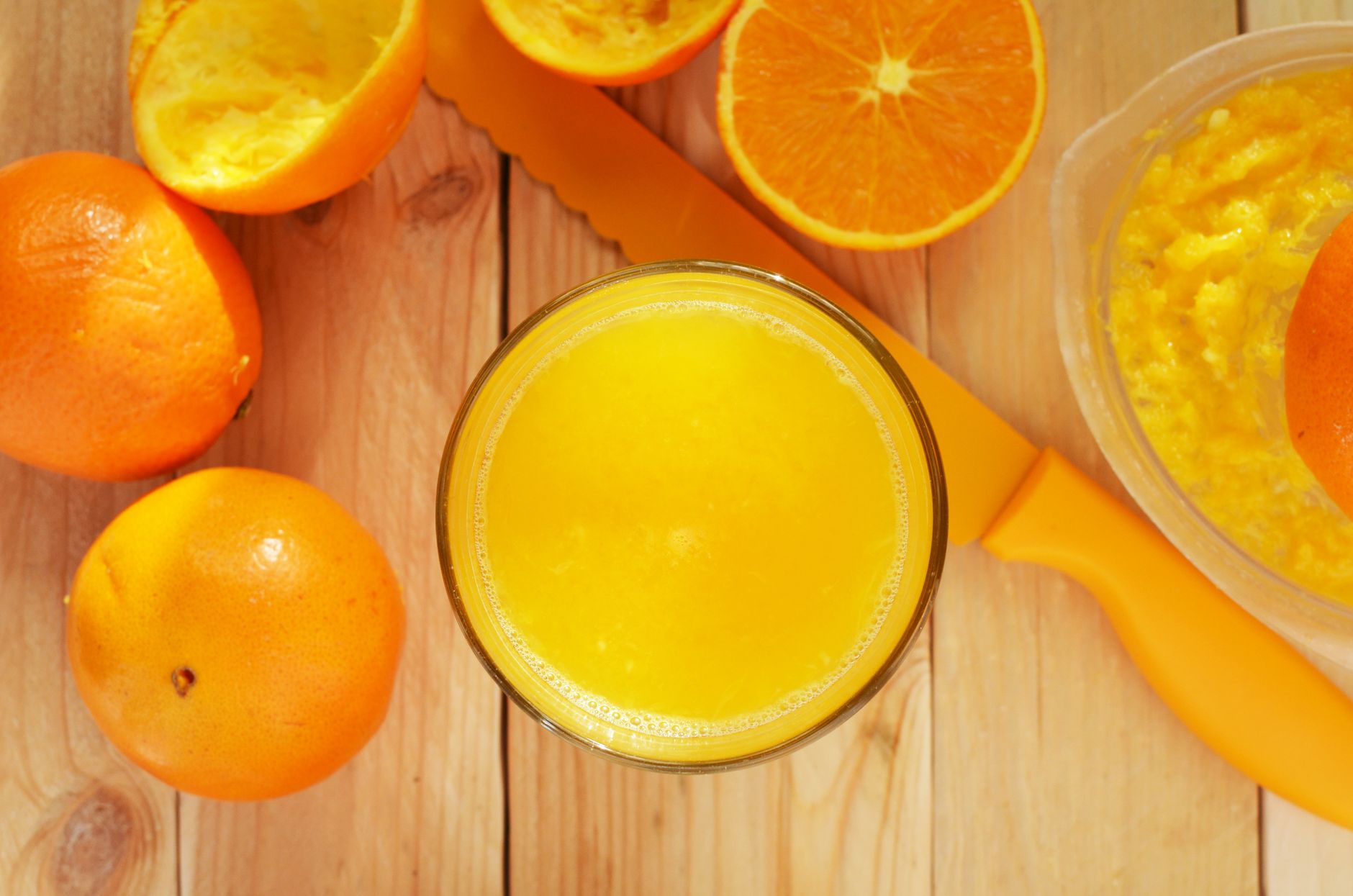 Glas frisch gepresster Orangensaft neben halbierten Orangen auf einem Holztisch