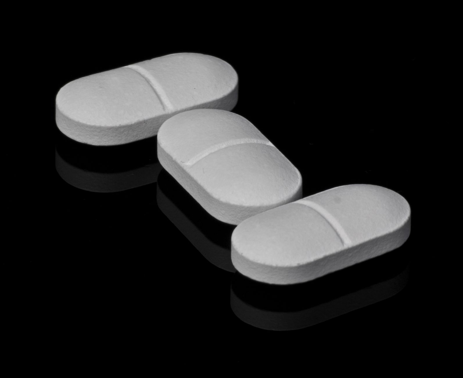 Three white tablets without embossing on a dark surface