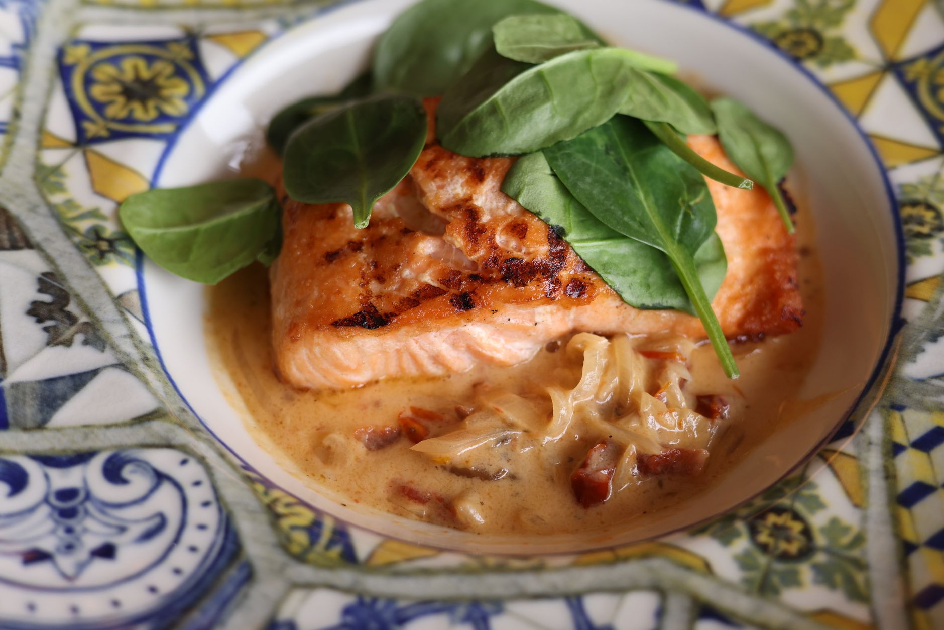 Filet de saumon cuit avec des feuilles d'épinards et une sauce sur une assiette à motifs