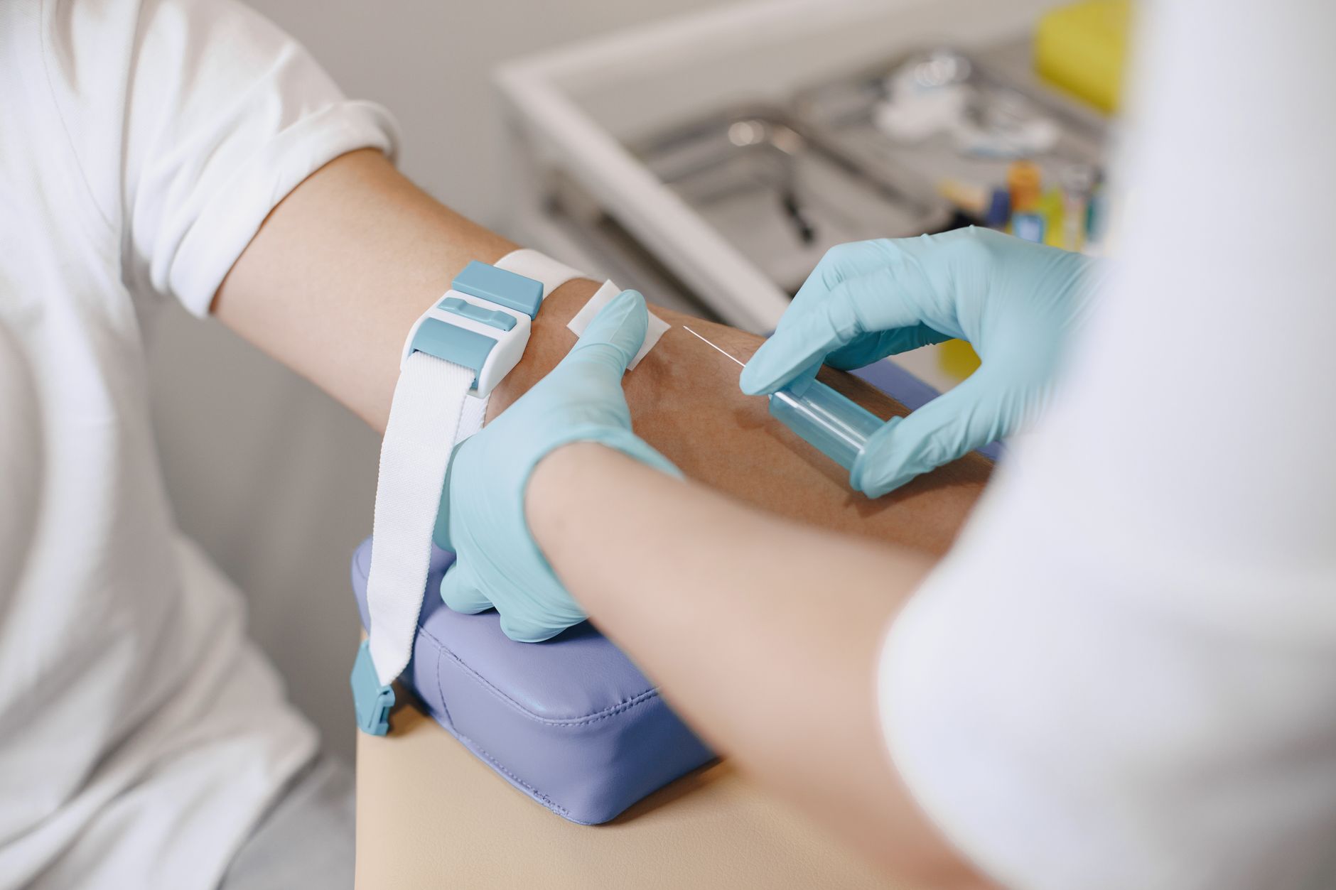 Blutentnahme am Arm: behandschuhte Hände setzen die Kanüle unterhalb des Stauschlauchs an.