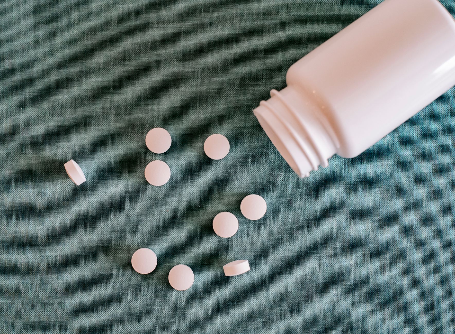 Weiße Tabletten neben einer umgekippten weißen Dose auf dunkelgrünem Stoff.