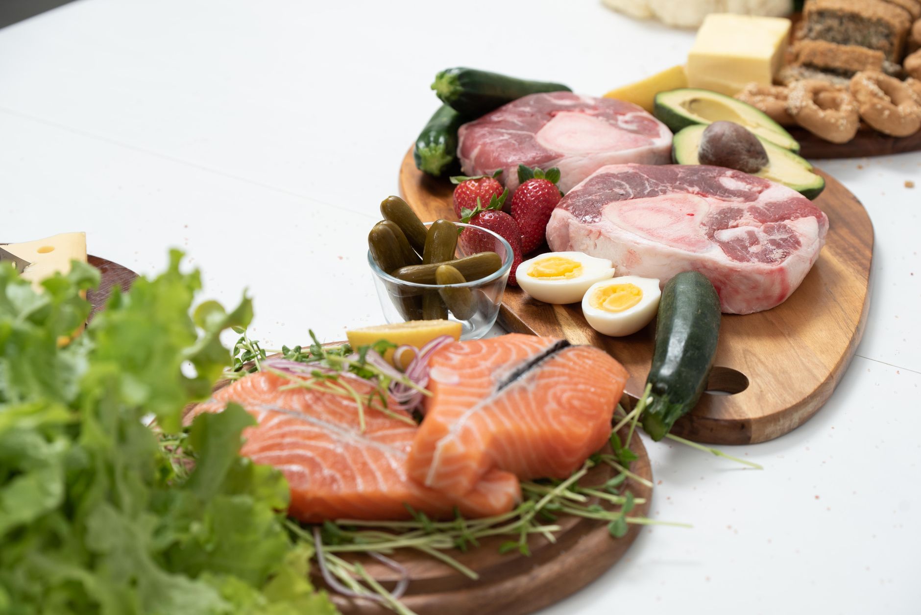 Rohe Lachsfilets, Rindfleisch, gekochte Eier und Käse auf hölzernen Schneidebrettern.