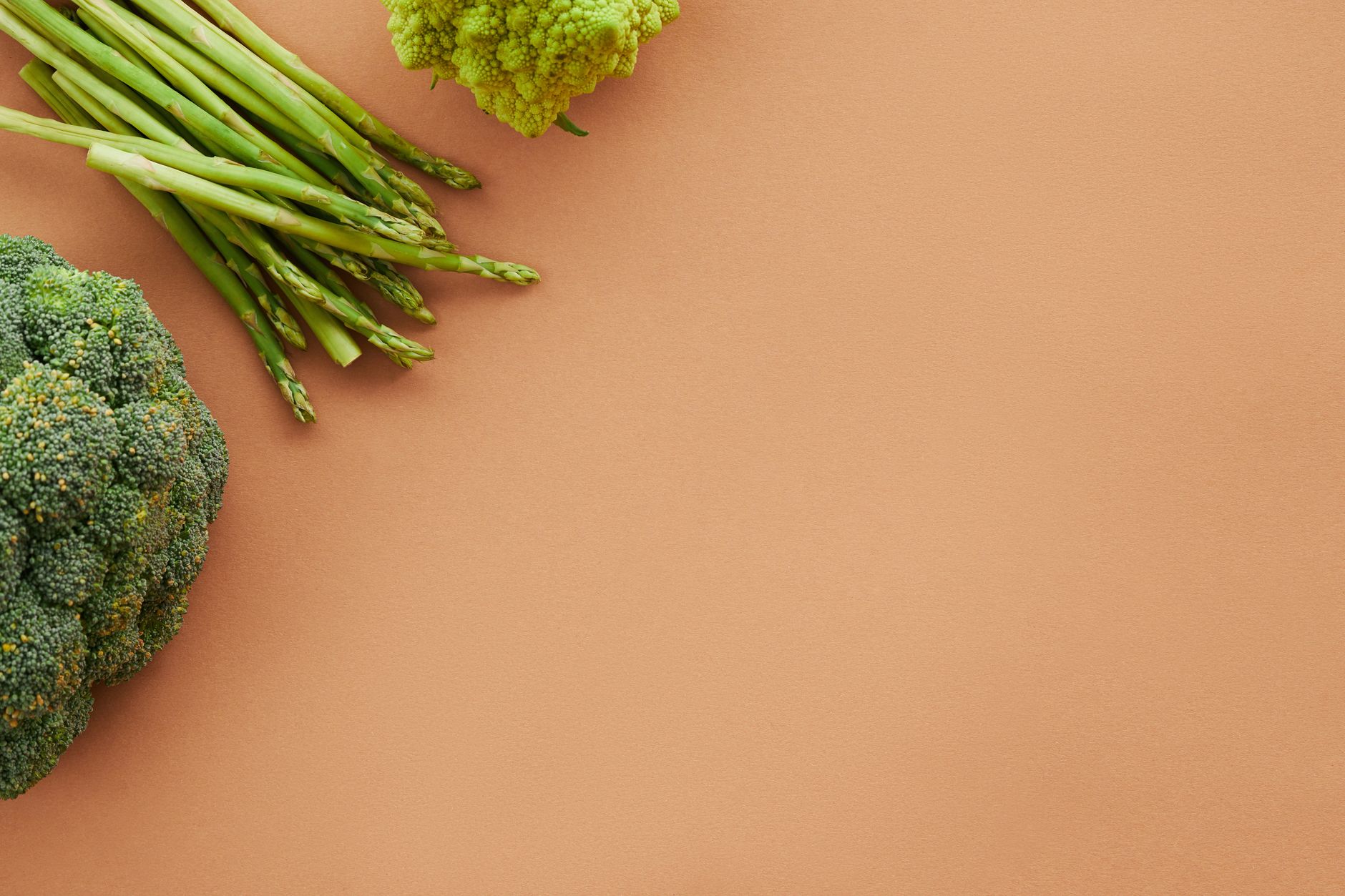 Asparagi verdi, broccoli e romanesco su un fondo color terracotta.