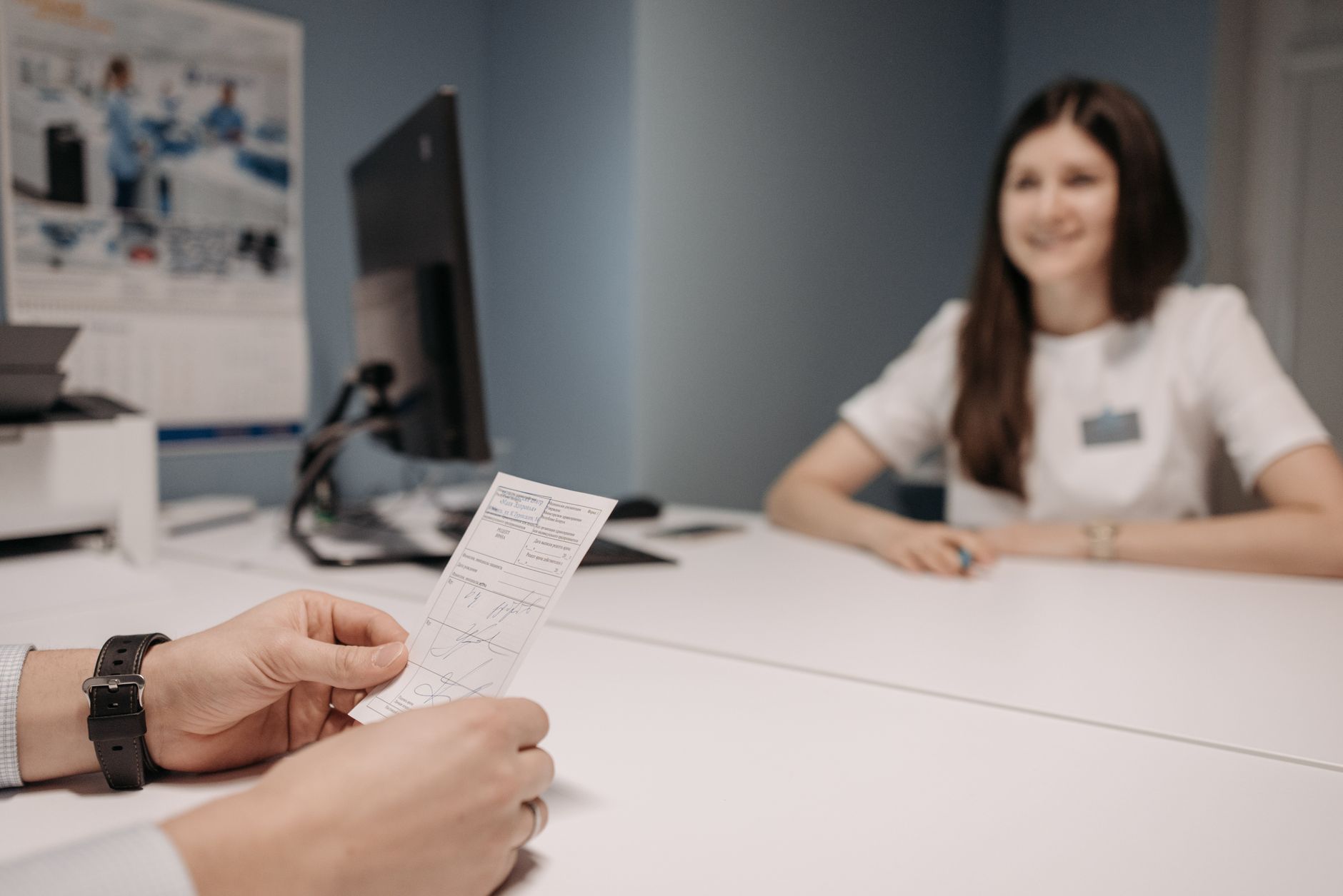 Ärztin am Schreibtisch, ein Patient hält ein Rezept in der Hand.