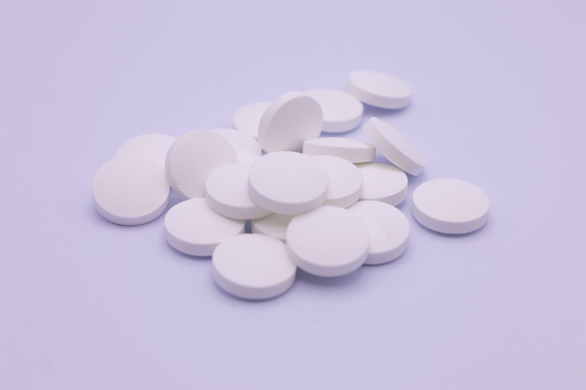 Weiße runde Tabletten, lose auf einer hellen Fläche liegend.