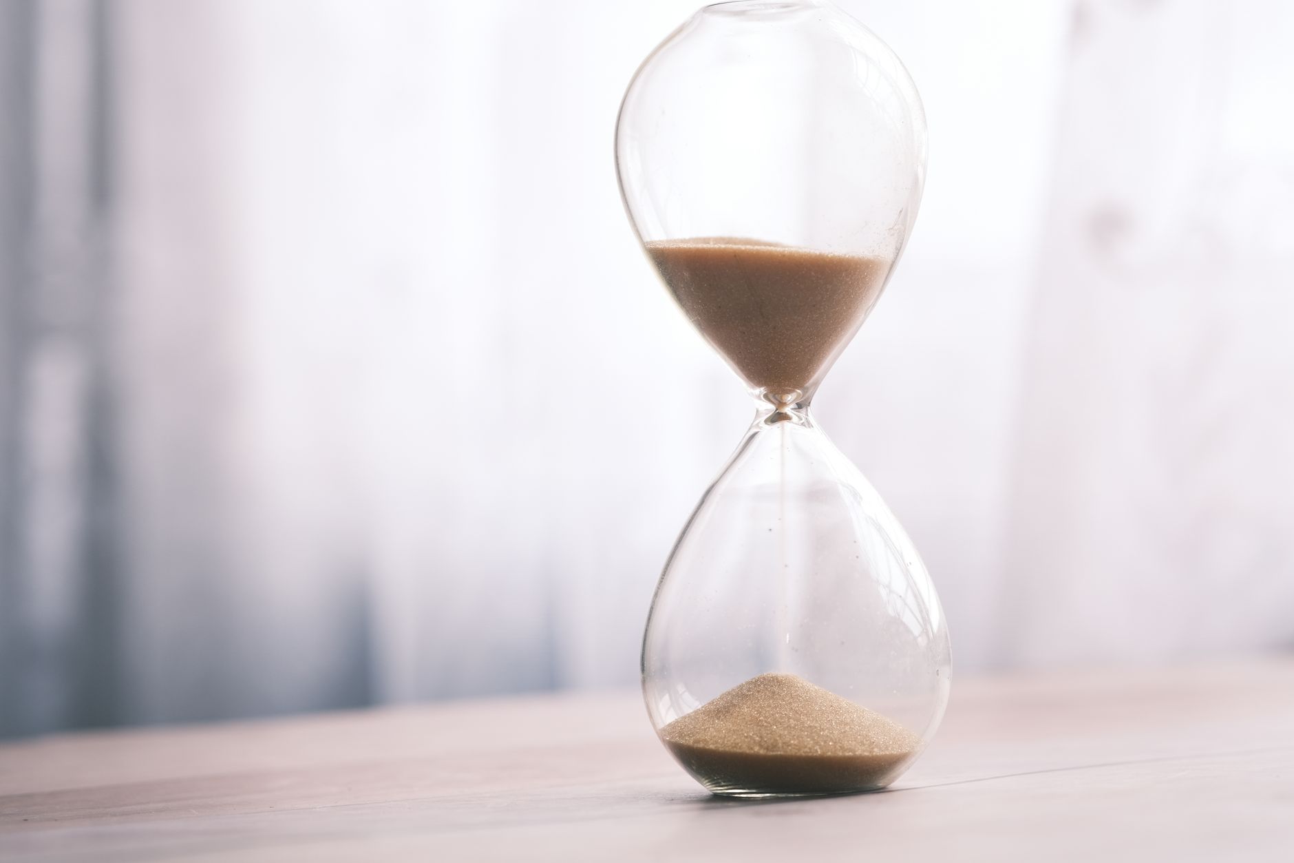 Sanduhr mit rieselndem Sand auf einer hellen Tischplatte.
