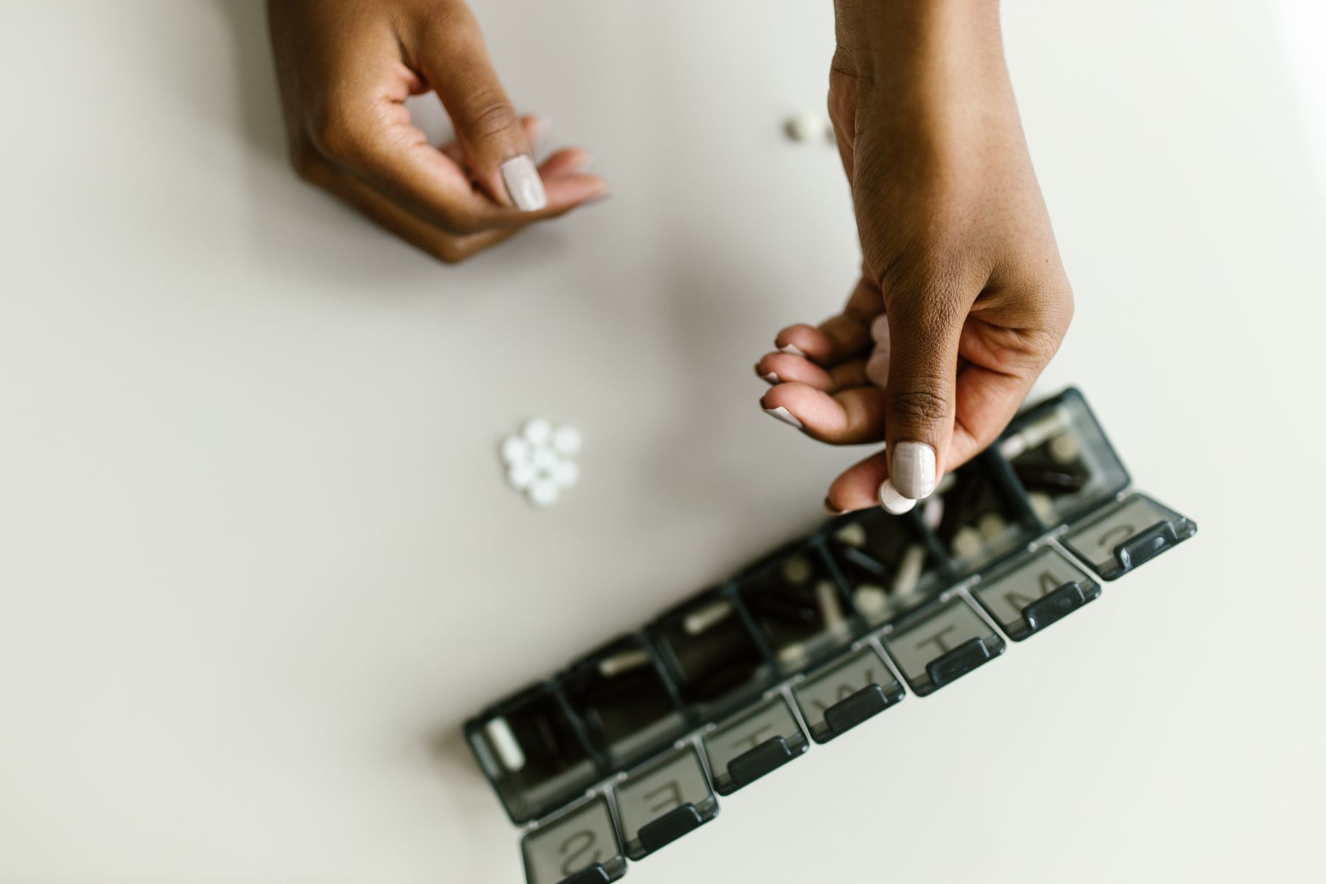 Hände sortieren Tabletten in eine Wochenbox mit Fächern für jeden Tag.