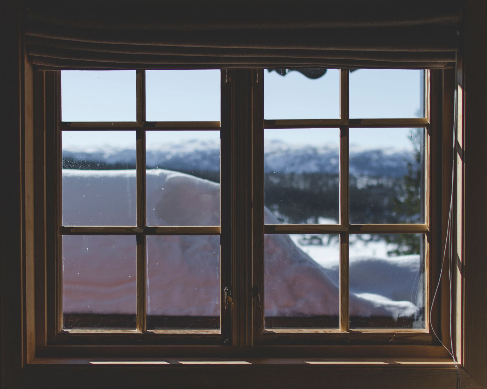 Blick durch ein Sprossenfenster auf eine verschneite Winterlandschaft.