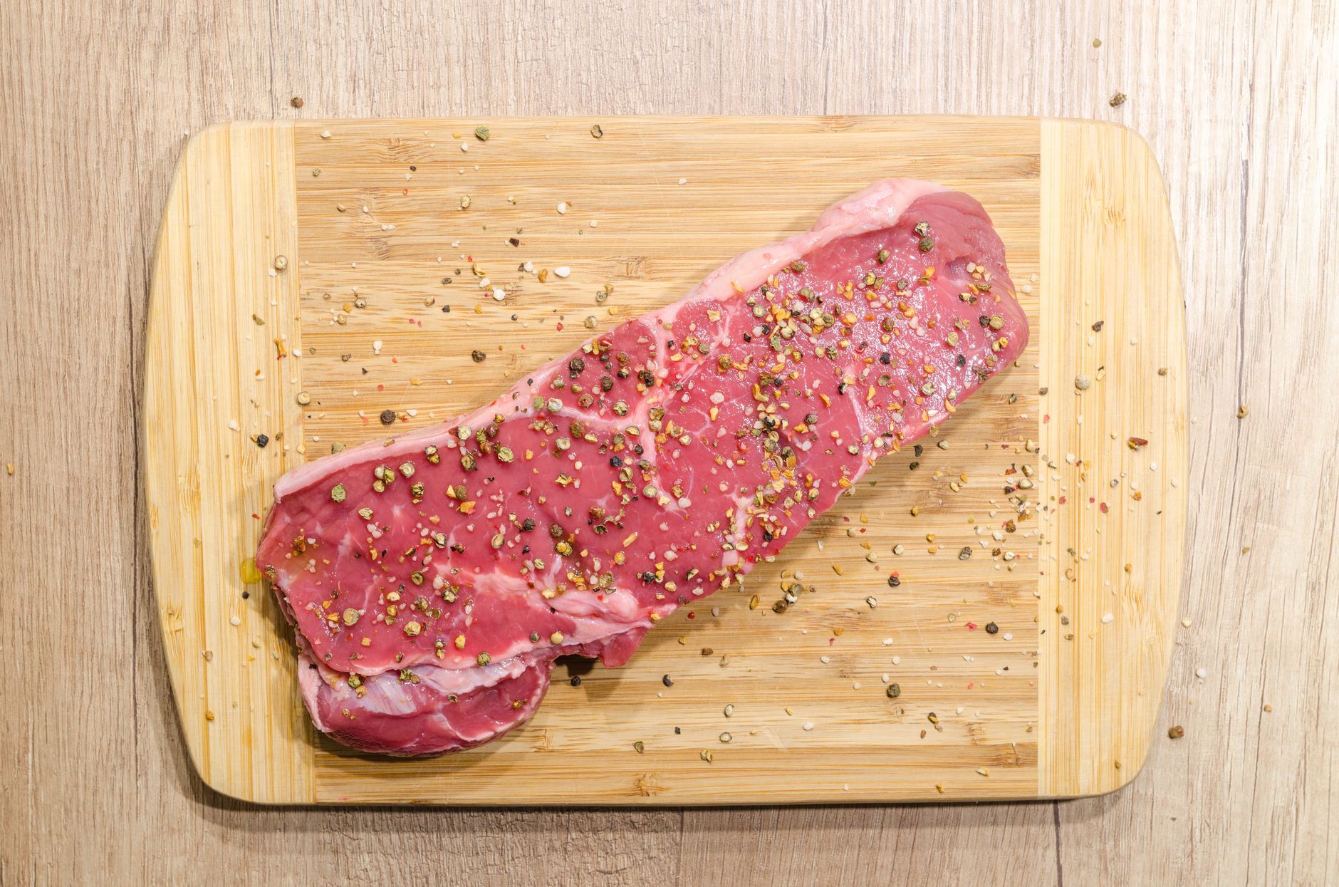 Rohes Rindersteak mit Pfeffer auf einem hellen Holzbrett