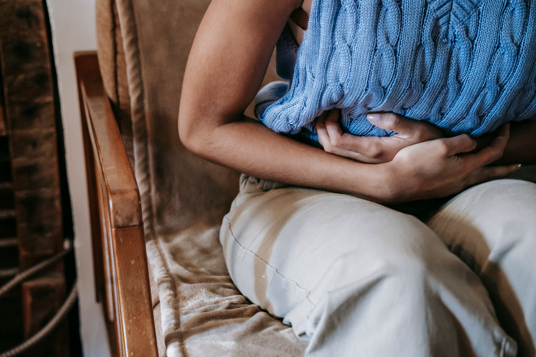 Person sitzt zusammengekrümmt auf einem Sessel und hält sich den Bauch